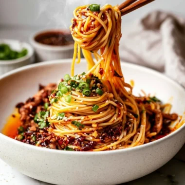 Bowl of cozy Szechuan noodles garnished with green onions and chili peppers