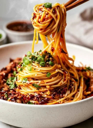 Bowl of cozy Szechuan noodles garnished with green onions and chili peppers