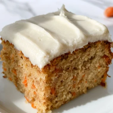 A slice of moist dairy-free carrot cake topped with cream and fresh carrots
