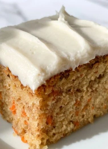 A slice of moist dairy-free carrot cake topped with cream and fresh carrots