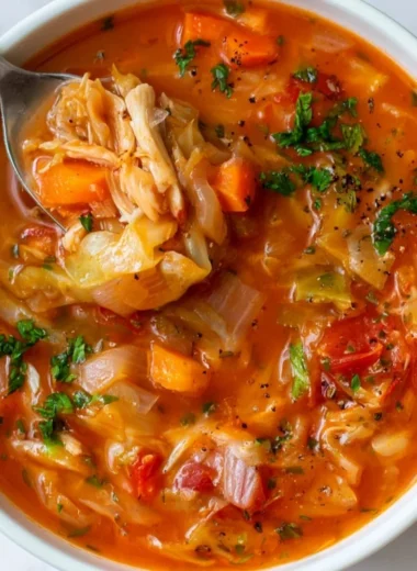 Bowl of warm, delicious cabbage soup garnished with herbs and vegetables